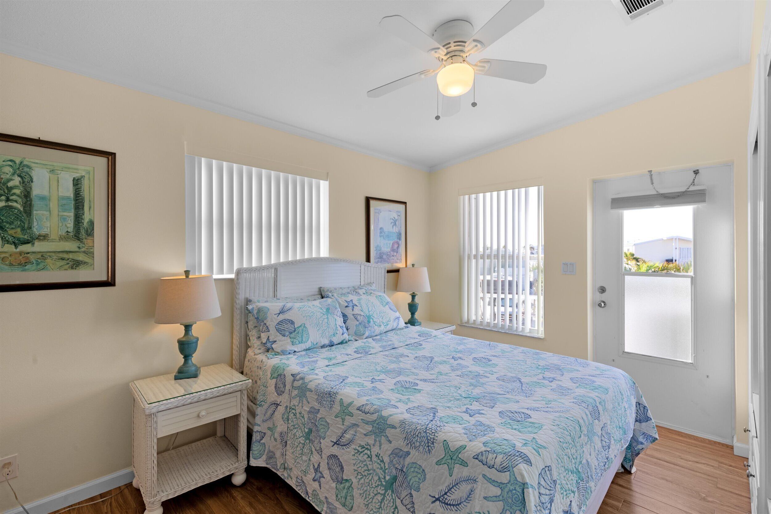 A bedroom with a bed, nightstands, a ceiling fan, and a door with a view.