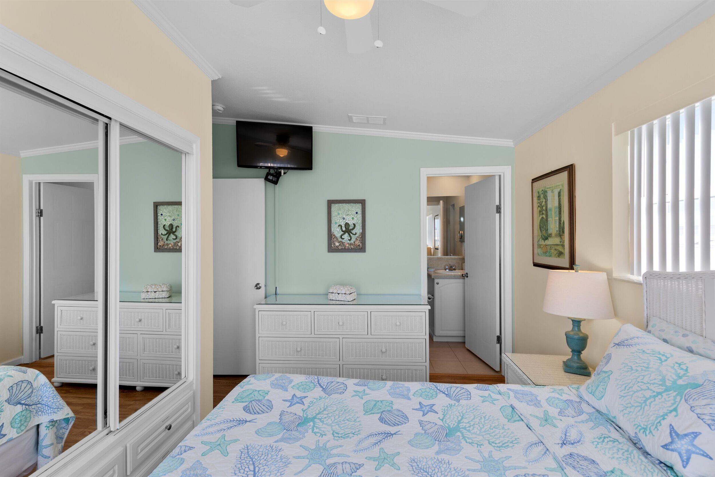 A bedroom with a bed, dresser, and a television on the wall.