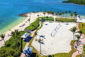 Vista aérea de una playa con aguas azul turquesa, palmeras y una cancha de tenis.