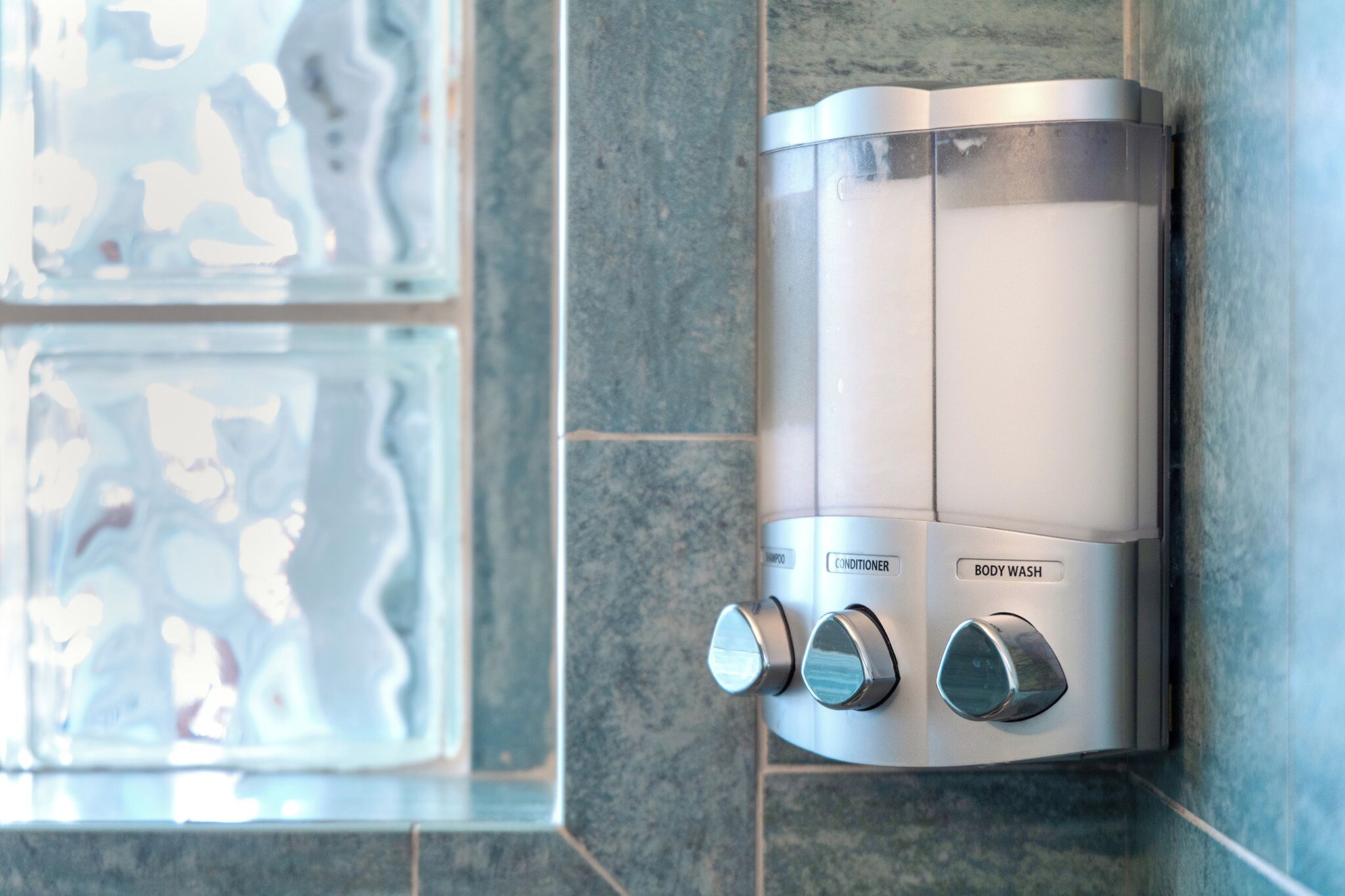 Un panneau de commande mural pour la douche, doté de boutons indiquant les fonctions « shampoing », « après-shampoing » et « gel douche ».