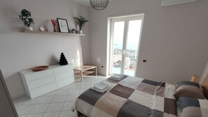 A modern bedroom with a large bed, a white dresser, a small table, and a balcony with a city view. - Dimora dei Naviganti - 15 Min from Amalfi Coast Sea View with Jacuzzi (Salerno)