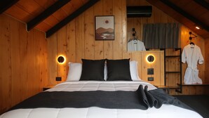 Quarto de cabana de madeira com cama, roupa de cama preta e branca, um quadro emoldurado com paisagem e um roupão pendurado em um suporte.