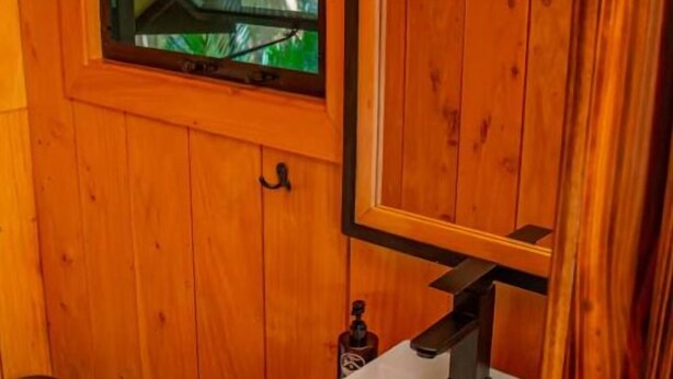Une salle de bain rustique, avec des murs en bois, un lavabo blanc, une fenêtre et un miroir.