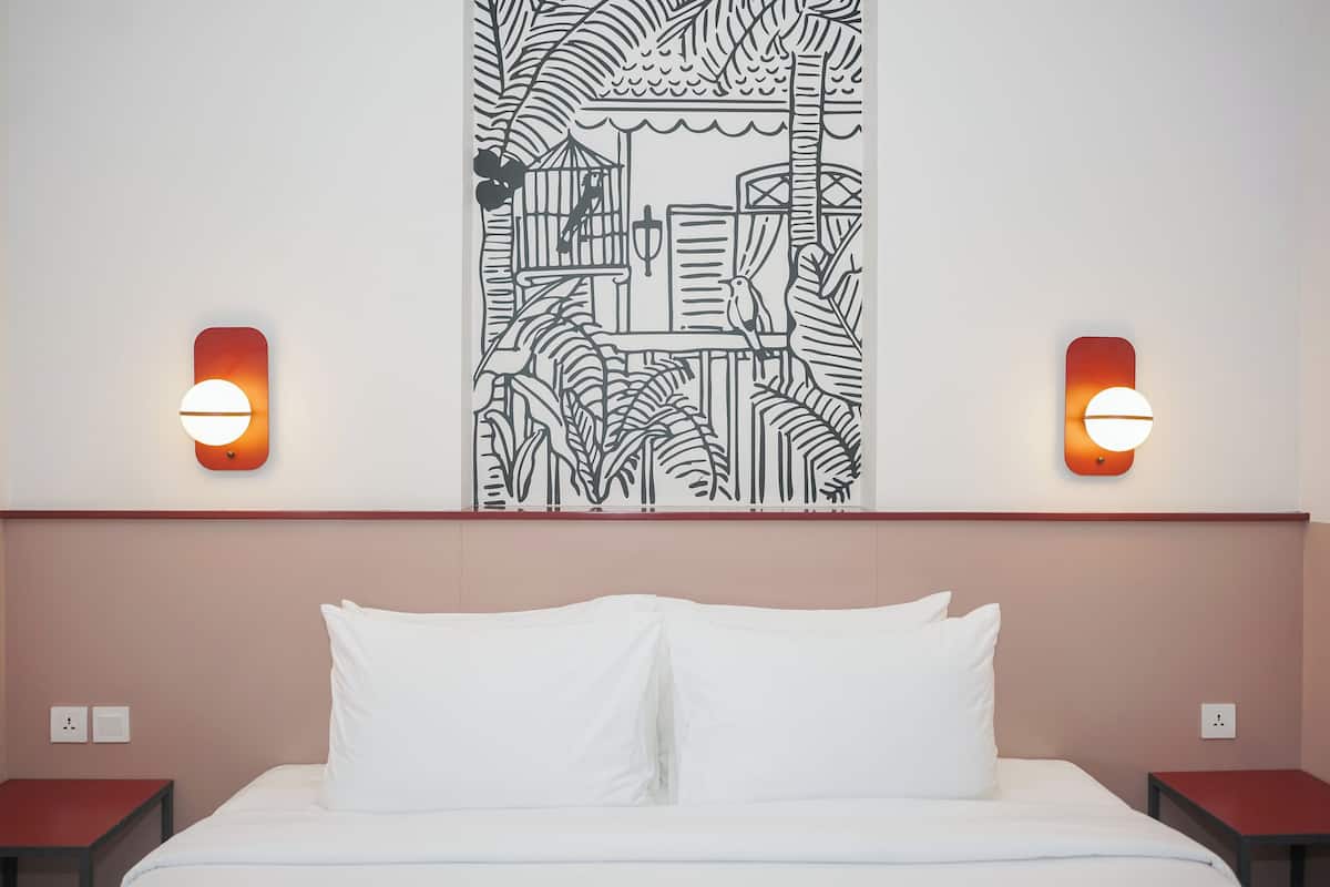 A hotel room with a bed, two nightstands, and a wall mural.