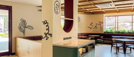 Interior de una cafetería moderna con mostrador central, zona de estar y decoración en la pared.