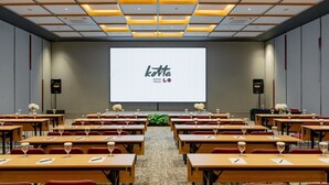 A conference room with rows of tables, a large screen displaying 'kotta HOTEL TEGAL', and speakers on either side. - Kotta GO Hotel Tegal (Tegal)