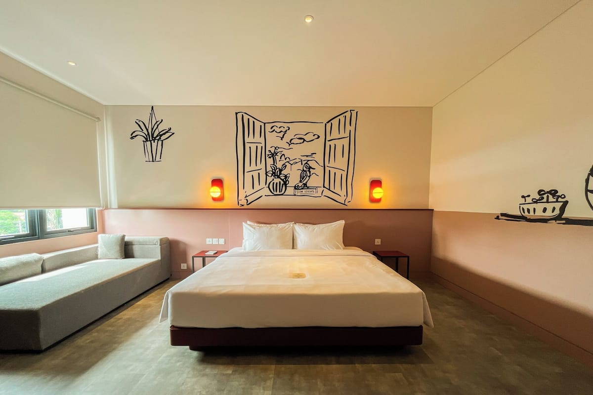 A modern hotel room with a large bed, a sofa, and a wall mural.