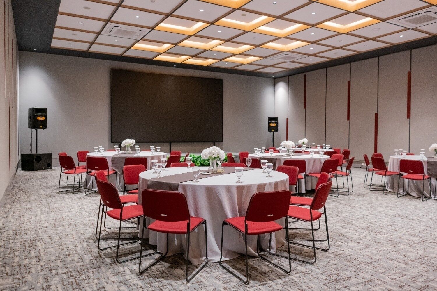 A conference room with round tables, red chairs, and a large screen.
