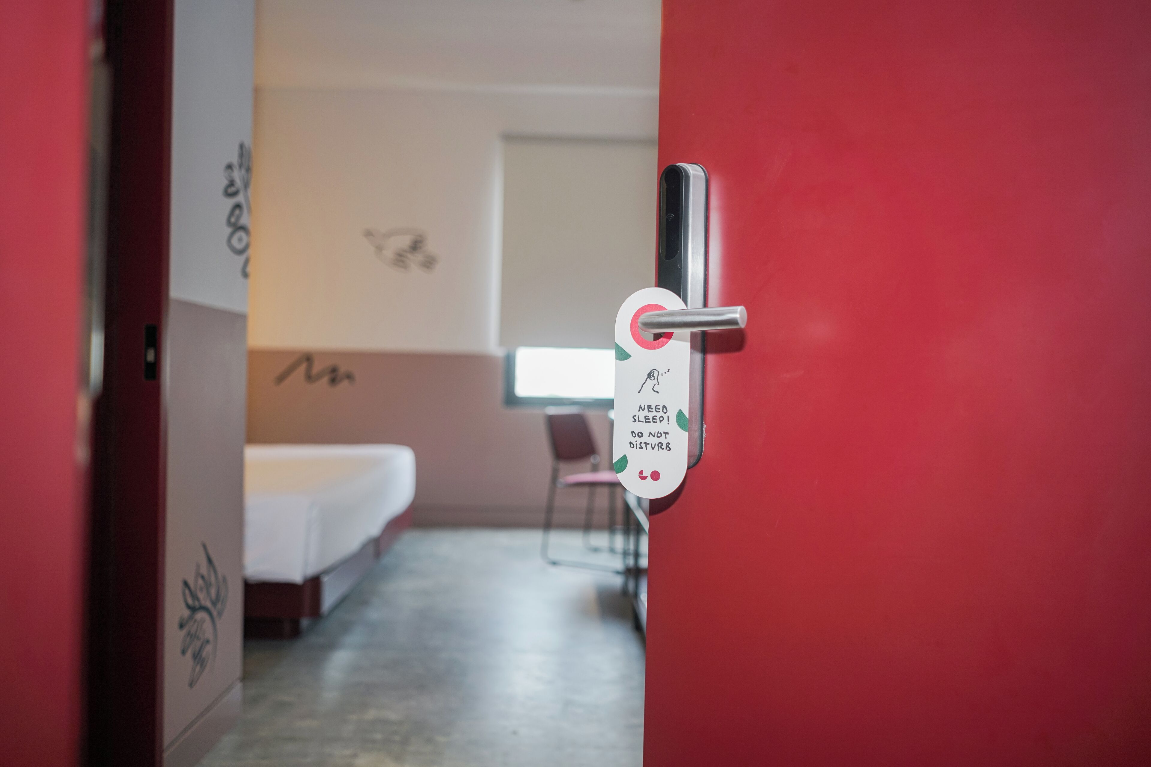Habitación de hotel con cama, una silla y una puerta con un cartel que indica la necesidad de descanso y pide no ser molestados.