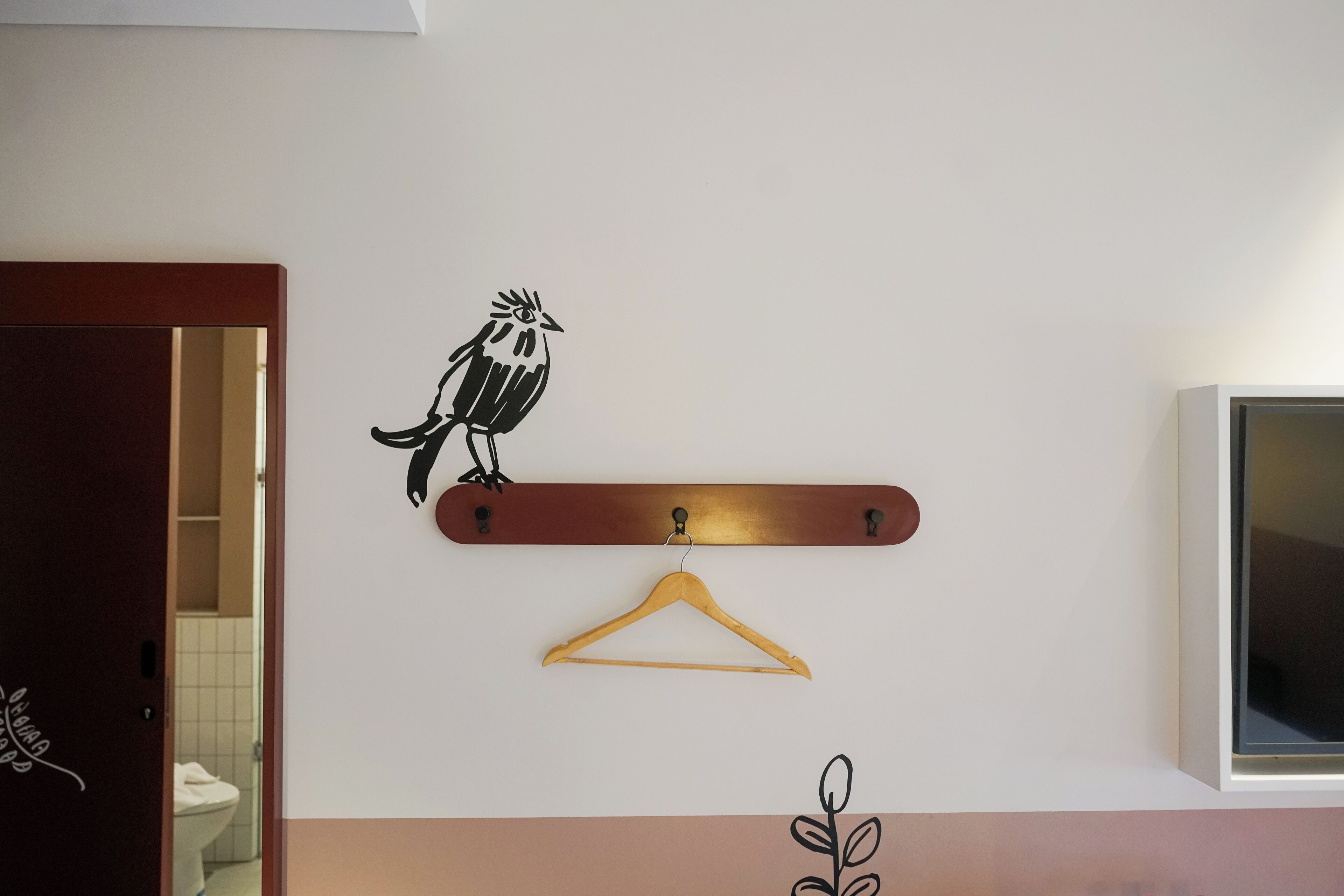 Ein an der Wand befestigter Holzhalter mit Vogelaufkleber, ein Holzregal darüber und ein Fernseher auf der rechten Seite.