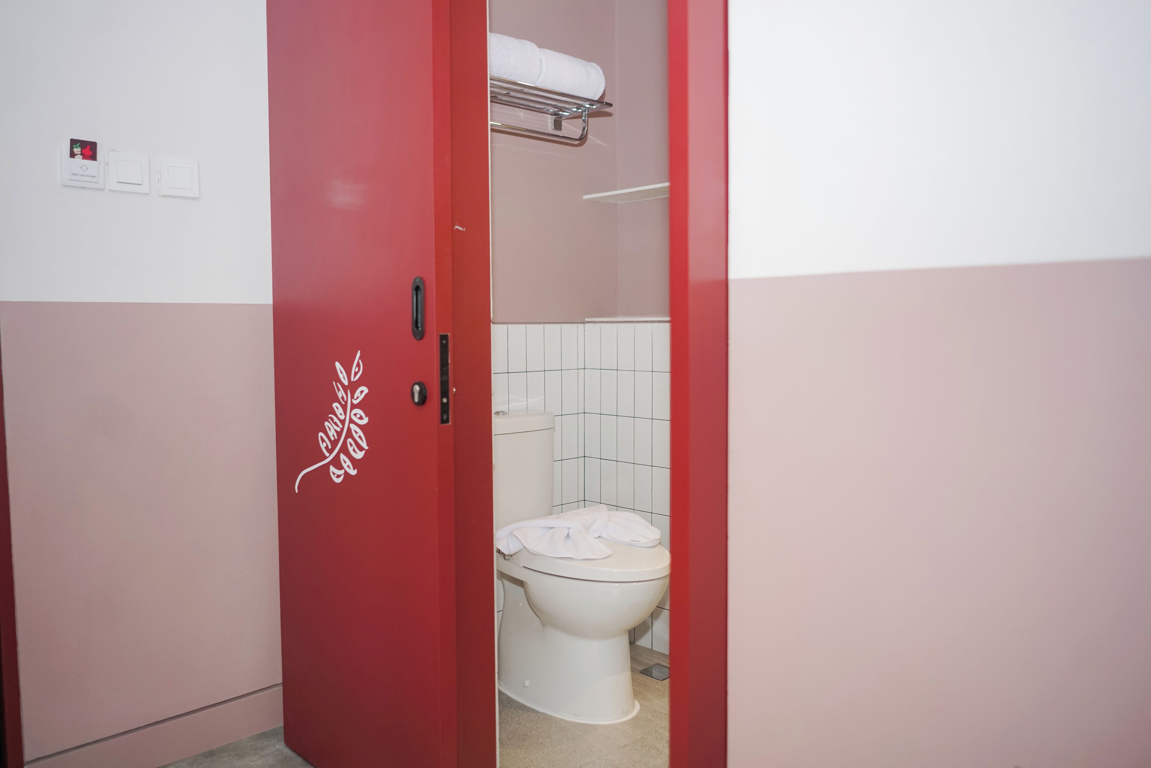 Ein Badezimmer mit einer weißen Toilette, einer roten Tür und einem Handtuchhalter über der Toilette.