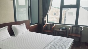 A hotel room with a large bed, a small table, two chairs, and a window with curtains. - Nha Nghi Thanh Binh 2 (Vinh Hung)