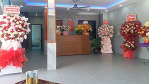 A reception area with a wooden desk, multiple flower arrangements, and signs indicating services. - Nha Nghi Thanh Binh 2 (Vinh Hung)
