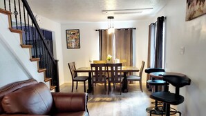 A dining area with a wooden table and chairs, a brown leather sofa, and a staircase with black railings.