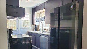 A modern kitchen with dark cabinets, a stainless steel refrigerator, and a window with a view of trees.