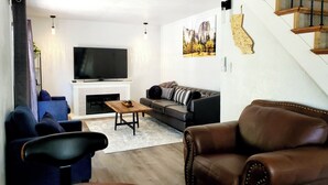 A modern living room with a fireplace, a large flat-screen TV, a sofa, and a leather armchair.