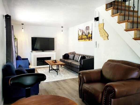 Una sala de estar moderna con chimenea, un televisor de pantalla plana grande, un sofá y un sillón de cuero.