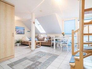 Un salon chaleureux avec un plafond haut, un ensemble de canapés, une table à manger et un escalier.