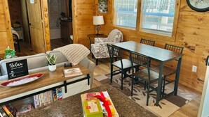 A cozy cabin interior with a dining table, chairs, a sofa, a small kitchen area, and a clock on the wall. - Majestic Woods Cabin 1 (Logan)