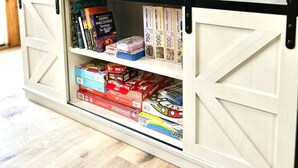Een houten interieur met een wit opbergmeubel gevuld met spelletjes en boeken.