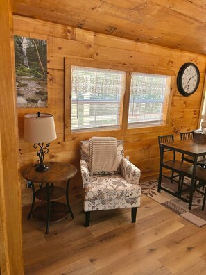 A cozy room with wooden walls, a chair, a table, and a clock. - Majestic Woods Cabin 1 (Logan)