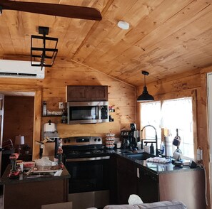 A wooden cabin interior with a kitchen area featuring a stove, microwave, and cabinets. - Majestic Woods Cabin 1 (Logan)