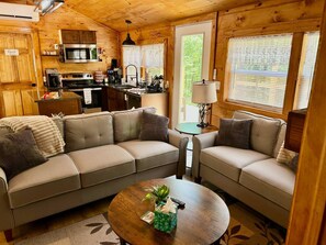 A cozy cabin-style room with a sofa set, a coffee table, and a kitchenette. - Majestic Woods Cabin 1 (Logan)