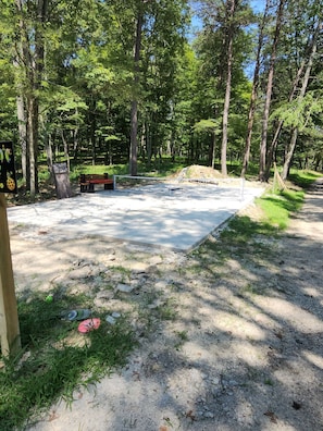 Un camping con zona de juegos de concreto, rodeado de árboles y zonas verdes.