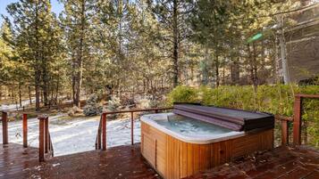 Une terrasse en bois avec un jacuzzi, le tout entouré d’une forêt.