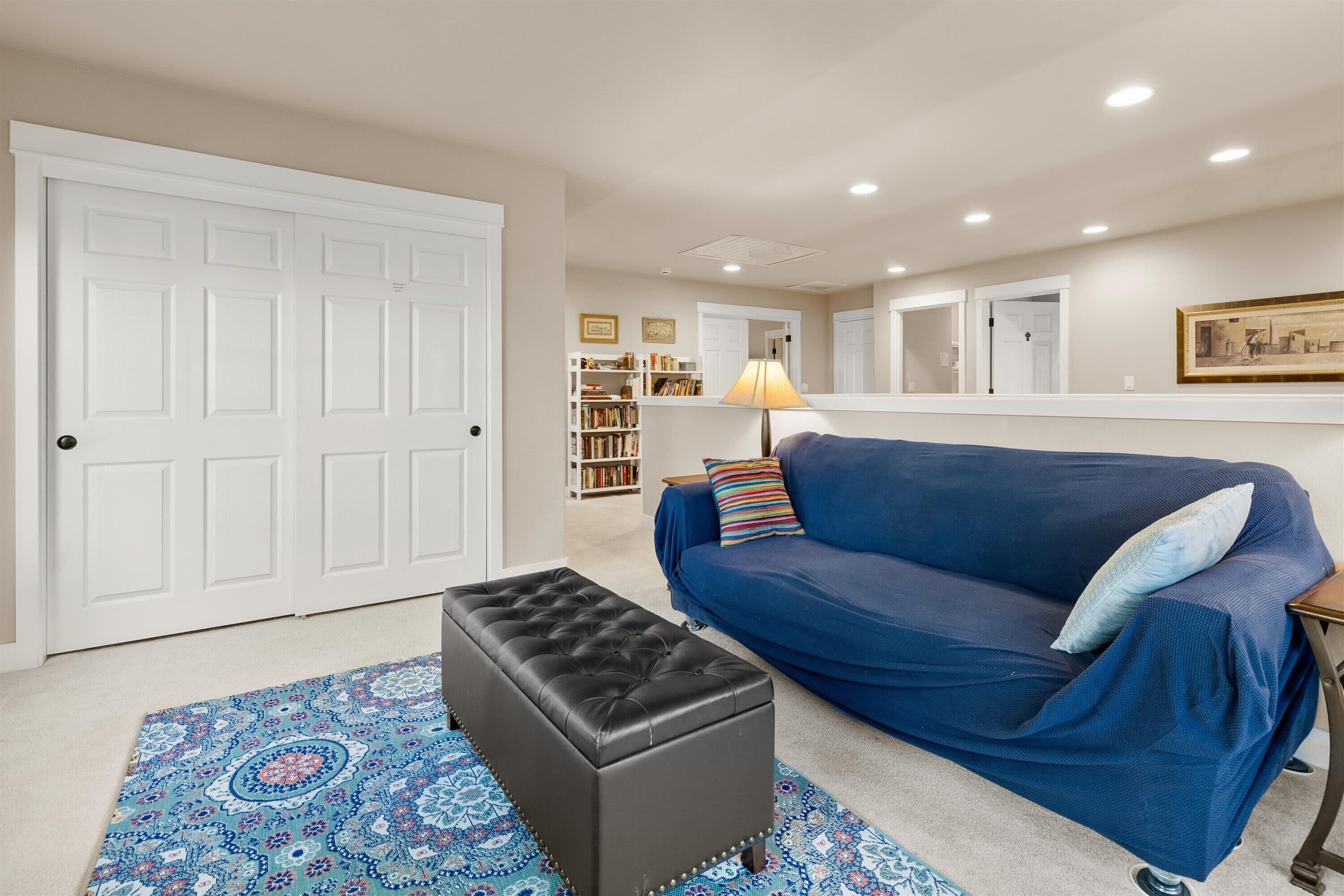 A living room with a blue sofa, a black ottoman, and a patterned rug.
