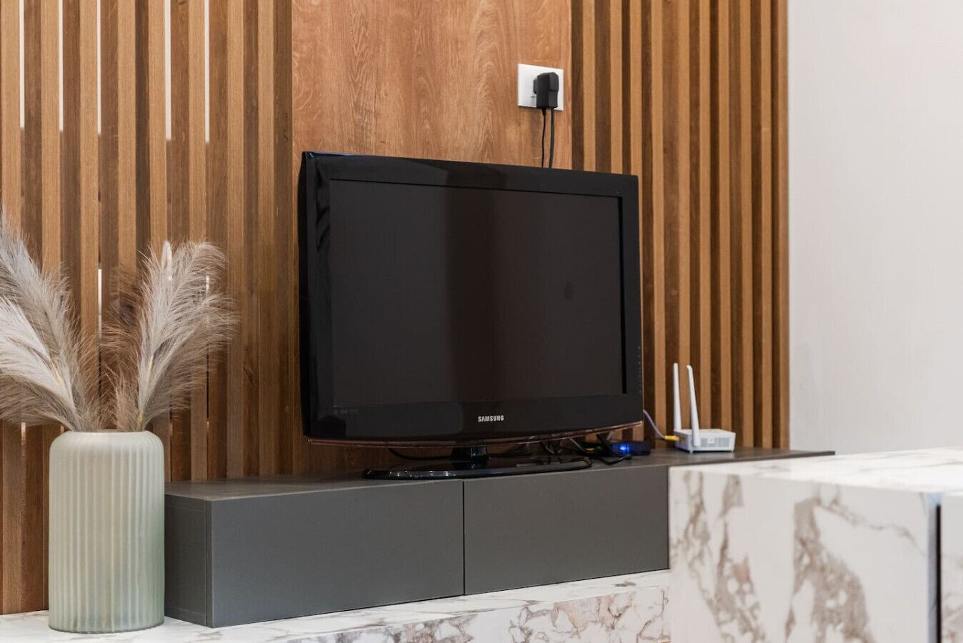 Un téléviseur Samsung fixé sur un mur en bois, avec une prise de courant blanche située juste au-dessus.