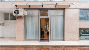 A building with a large glass door entrance, a small air conditioning unit on the left, and a staircase on the right.