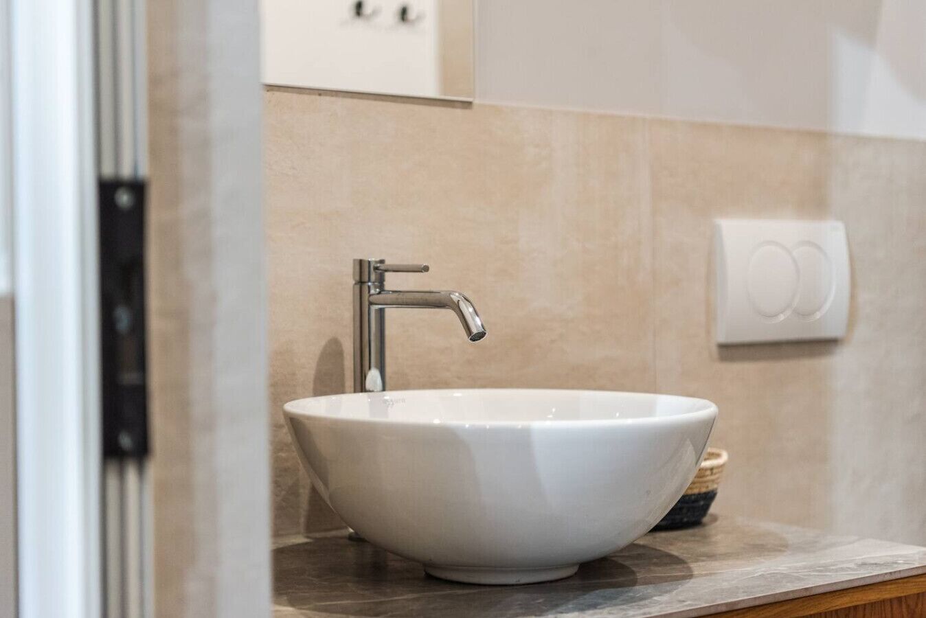Un baño con un lavabo blanco tipo recipiente, un grifo moderno y un interruptor de luz en la pared.
