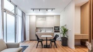 A modern apartment with a dining area, kitchen, and a large window.