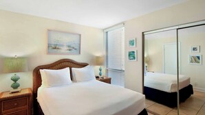 Une chambre à coucher avec un grand lit, une table de chevet avec une lampe, un miroir et une fenêtre avec des stores.
