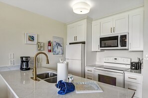 A modern kitchen with white cabinetry, a stainless steel sink, a coffee maker, a microwave, and an oven.