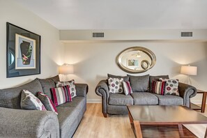 A living room with two grey sofas, a coffee table, and a round mirror on the wall.