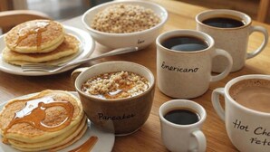 A breakfast setting with pancakes, oatmeal, and coffee cups on a table.