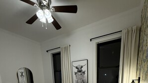 A bedroom with a bed, a ceiling fan, a window with curtains, a dresser, and a framed picture on the wall.