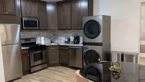 A modern kitchen with dark wood cabinets, stainless steel appliances, a black dining table with pink chairs, and a ceiling fan.