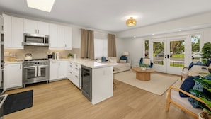 A modern kitchen with white cabinets, a built-in oven, and a microwave. There is a dining area with a wooden table and chairs, and a large window offering a view of the street. - New 2 En Suite Bedrooms, Balboa Park,  Lux, 85" TV, Parking! (San Diego)