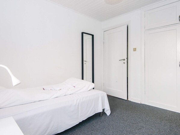 Una habitación pequeña y limpia con una cama individual, un escritorio blanco y dos puertas blancas.
