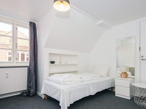 A bedroom with a bed, a bedside table, a mirror, and a window with curtains.