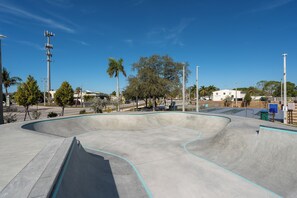 A skate park with a large concrete bowl, surrounded by trees and a clear blue sky.