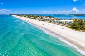A coastal beach with clear turquoise waters, a sandy shoreline, and buildings along the beach.