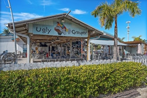 A building named 'Ugly Grouper' with outdoor seating and a palm tree in the foreground.