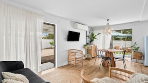 En moderne stue med en sort sofa, fletstole, et spisebord og et fjernsyn ophængt på væggen.