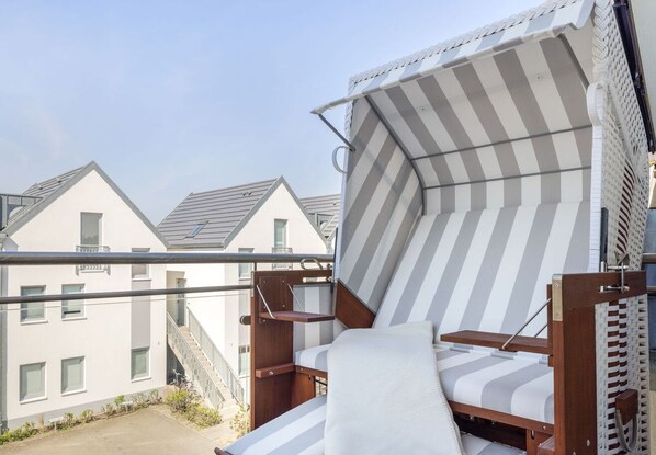 Un balcon avec un auvent rayé et une chaise en bois.