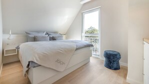 A bedroom with a bed, a bedside table, a chair, and a view of the outdoors. - Dünenloft - Relax and enjoy in the Dünenloft: your perfect vacation apartment on the (Rantum)