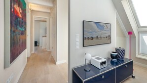 A modern interior with a hallway leading to a bedroom, a large painting, a framed beach photo, and a desk with a radio. - Dünenloft - Relax and enjoy in the Dünenloft: your perfect vacation apartment on the (Rantum)